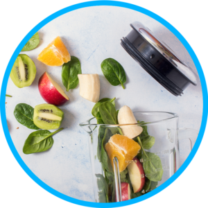 A top view of kiwi, spinach, orange, apple and bananas spilling out of a blender with a glass bowl and silver top.